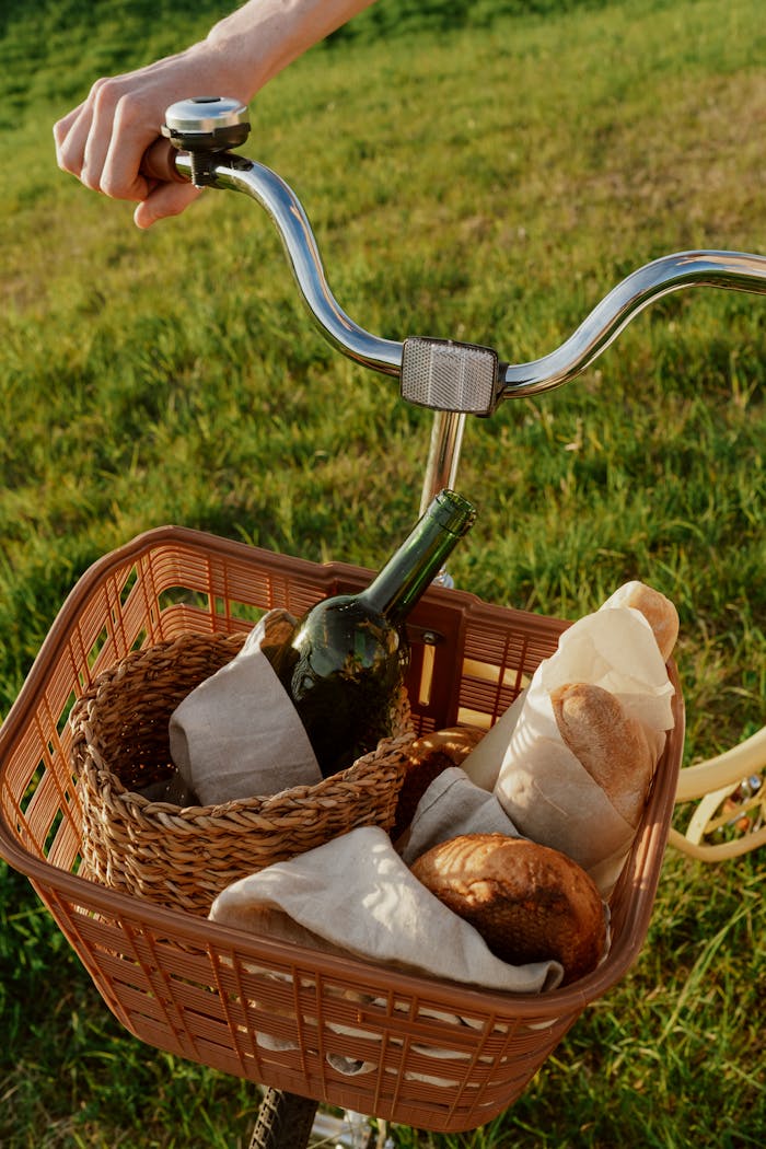 Bicycle basket in a meadow with wine and bread, perfect for a summer picnic.