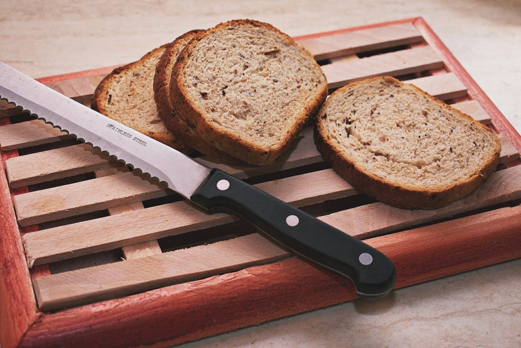 Freshly sliced whole grain bread on a wooden board with a stainless steel knife.